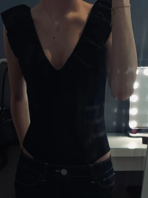 Svart body med volang & v-ringad  - Snygg svart body med djup v-ringning och  volangdetaljer längs axlar. Matchar till allt möjligt. Inga defekter alls, jättefint skick! 🫶🏼