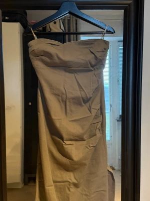 Grön axelbandslös klänning Zara - Säljer en beige axelbandslös klänning från Zara. Klänningen har figurnära passform och är i ett mjukt bomullsmaterial. Perfekt för dig som gillar minimalistisk stil och vill ha en enkel men snygg look.