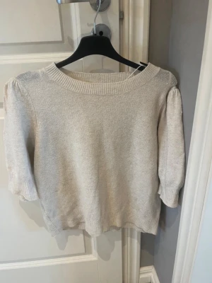 Beige stickad tröja från ONLY - Snygg beige stickad tröja från ONLY med puffärmar och bred ribbad halsringning. Tyvärr lite nopprig,