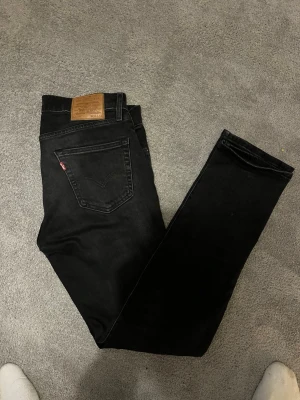Levis 511 - Säljer ett par svarta jeans från Levi's med klassisk rak passform. Jeansen har fem fickor, Levi's ikoniska läderpatch bak och röd etikett på bakfickan. Tillverkade i slitstark denim som ger en snygg och tidlös look.