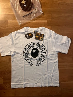 Vit A Bathing Ape t-shirt - Snygg vit t-shirt från A Bathing Ape med det klassiska stora aptrycket framtill och coola grafiska detaljer. T-shirten har rund hals och korta ärmar. Tillverkad i mjuk bomull och levereras i originalförpackning med taggar kvar.