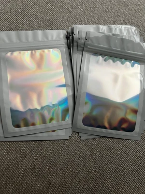 20st Holografiska zip-påsar, 15x10 cm - Säljer 20 stycken holografiska zip-påsar i plast med silvrig baksida och regnbågsskimrande framsida. Perfekta för förvaring av småprylar, smycken eller presenter. Påsarna har återförslutningsbar öppning och är flexibla och tåliga. Storlek: 15x10cm