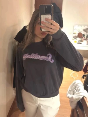 Mörkgrå sweatshirt med tryck - Mörkgrå sweatshirt med lila texttryck framtill. Tröjan har rund hals, långa ärmar och ribbade muddar vid ärmslut och nederkant. Den har en liten fläck.💕