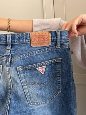 Blå bootcut jeans från Guess - Säljer ett par klassiska blå bootcut jeans från Guess med ikoniska märket på bakfickan. Det är ett år riktiga favoriter från min garderob som tyvärr blivit för små. De är helt perfekta i tvätten! 