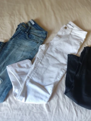 Tre par jeans i olika färger - Säljer tre par jeans i olika färger: ett par klassiska blå jeans, ett par vita jeans och ett par svarta jeans. Alla har femficksmodell och normal midja. Perfekta för dig som vill variera din stil med basfärger i garderoben.
