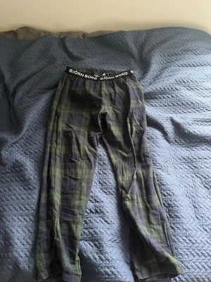 Rutiga pyjamasbyxor från Björn Borg - Mysiga pyjamasbyxor från Björn Borg i grönt och mörkblått rutigt mönster. Byxorna har resår i midjan med Björn Borg-logga och är tillverkade i mjukt tyg, perfekta för chillkvällar hemma.