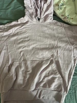 Ljuslila hoodie med huva - En ljuslila hoodie med stor känguruficka framtill och ribbade muddar vid ärmslut och nederkant. Hoodien har dragsko i huvan och är gjord i mjukt bomullsliknande material.