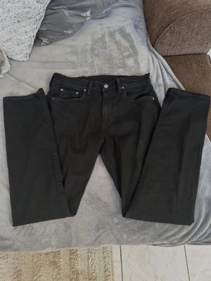 Svarta raka jeans från Levi's - Säljer ett par klassiska svarta jeans från Levi's med rak passform och fem fickor. Jeansen har silverfärgade nitar och knapp, samt den ikoniska röda Levi's-lappen bak. Tillverkade i slitstark denim med bälteshällor och normal midja.  Ny pris:1600kr