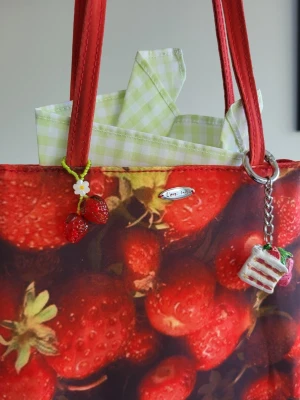 Strandväska/picknickväska med jordgubbstryck - Köpt från papi luv, inga defekter, aldrig använd, bra kvalitet. 🥰🥰Jordgubbsmotiv, två dekorativa berlocker, en med jordgubbar och en med en tårtbit.. Perfekt för dig som gillar unika accessoarer med somrig känsla, för midsommar eller picknickar.