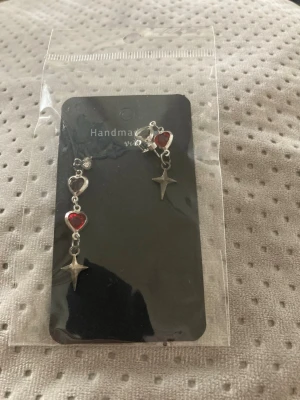 Silvriga örhängen med röda hjärtan - Säljer ett par handgjorda silvriga örhängen med röda hjärtformade detaljer och hängande stjärnor. Örhängena har en cool och unik design som sticker ut. Perfekta för dig som gillar att addera lite extra till din look.