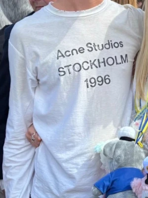 Vit långärmad t-shirt Acne Studios - Vit långärmad topp från Acne Studios med tryck 'Acne Studios STOCKHOLM 1996' på bröstet. Klassisk rund halsringning och relaxed fit. Perfekt för dig som gillar minimalistisk och stilren design.