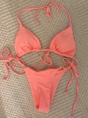 Korall bikini med knyt - Snygg korall färgad bikini med trekants-bh och knyt i både topp och trosa. Helt oanvänd!!! Råka beställa 2 av samma så det är därför jag säljer.