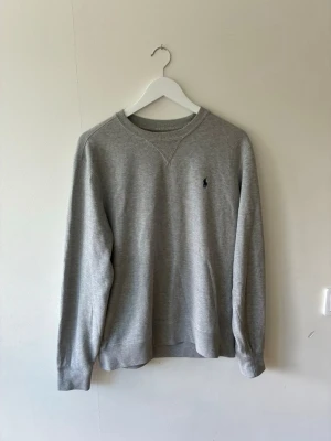 Grå sweatshirt från Ralph Lauren - Klassisk grå tröja från Ralph Lauren med rund halsring. Tröjan har ribbade muddar vid ärmslut och nederkant. Tröjan är i storlek Medium och är väldigt lätt buren. Tyvärr har texten i nacken åkt bort men man ser fortfarande märken och lite text så den är ändå äkta.