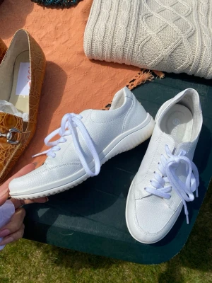 Vita sneakers från Rieker - Fräscha vita sneakers från Rieker med klassisk låg design. Skorna har vita snören, diskret logga på innersulan och ovandel i strukturerat syntetmaterial som ger en clean look. Perfekta för dig som gillar stilrena och bekväma sneakers.