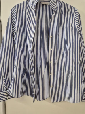 Skjorta - Klassisk skjorta från chico's i blåvitt randigt mönster. Skjortan har lång ärm, knappar framtill och en avslappnad passform. För en skön känsla och stilren look.