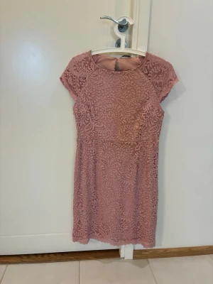 Rosa spetsklänning med kort ärm - Söt kort rosa klänning från ONLY med vackert spetsmönster över hela plagget. Klänningen har rund halsringning, korta ärmar och en figurnära passform. Perfekt för sommarens alla tillfällen!