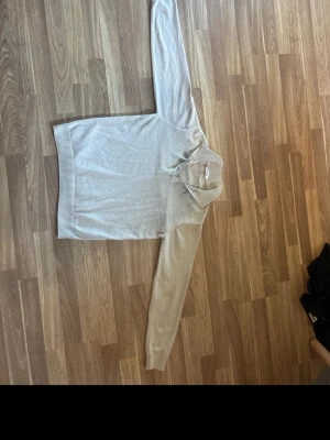 Beige stickad tröja med krage - Snygg beige stickad tröja med klassisk krage och långa ärmar. Tröjan har ribbade muddar vid ärmslut och nederkant, vilket ger en stilren look. Perfekt för dig som gillar en enkel men trendig stil. Materialet känns mjukt och bekvämt.