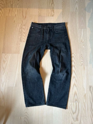 Svarta raka jeans från Cheap Monday - Säljer ett par svarta jeans från Cheap Monday med rak passform och klassisk femficksdesign. Jeansen har en lila logopatch bak i midjan och är tillverkade i denim. Perfekta för dig som gillar en clean och stilren look. 30/32
