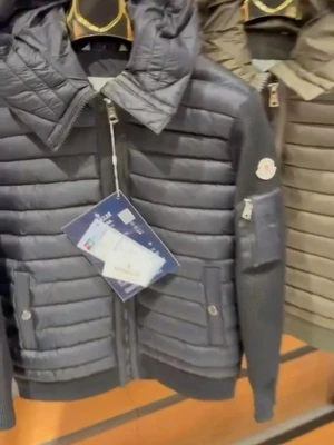 Svart pufferjacka från Moncler - Snygg svart pufferjacka från Moncler med quiltad design och huva. Jackan har dragkedja framtill, två fickor med lock och dragkedjeficka på ärmen med Moncler-logga. Ärmarna är i ett stickat material som ger en cool kontrast till det blanka tyget.