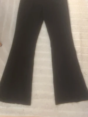 Svarta utsvängda kostymbyxor Gina Tricot -  Strlk xs men passar s de är ganska stora i storleken. Snygga svarta kostymbyxor från Gina Tricot med utsvängda ben och låg midja. Klassisk design utan synliga fickor framtill, perfekta till en trendig look. Materialet känns mjukt och följsamt, vilket ger en skön passform.