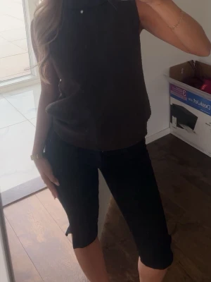 Svarta capri byxor - Säljer ett par svarta knälånga shorts med midwaist passform. Shortsen har en enkel och stilren design utan synliga detaljer och passar perfekt till sommaren. Materialet känns mjukt och bekvämt.