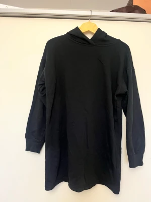 Svart oversized hoodie - En svart oversized hoodie med lång ärm och huva. Hoodien har en enkel och clean design utan tryck eller detaljer, och är tillverkad i ett mjukt bomullsliknande material. Perfekt för en avslappnad och chill stil.
