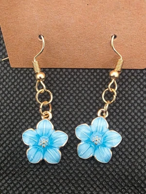 Handgjorda blå blomformade örhängen - Snygga handgjorda örhängen med blå blommor i resin och guldfärgade metalldetaljer. Blommorna har fem kronblad och små silverfärgade prickar i mitten. Perfekta för dig som vill ha en färgklick till din outfit.