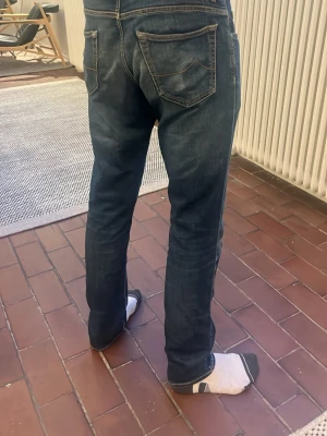  Jacob Cohën  jeans mörkblå med slitning - Säljer ett par mörkblå Jacob Cohën med klassisk femficksdesign och en riktigt fet slitning på ena benet. Jeansen har raka ben och kontrastsömmar. Perfekt för dig som gillar en avslappnad och cool stil. Patchen har fet slitning