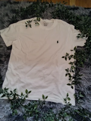 Vit t-shirt från Polo Ralph Lauren - Vit t-shirt från Polo Ralph Lauren med klassisk svart broderad logga på bröstet. T-shirten har rund hals och korta ärmar, perfekt för dig som gillar stilrena basics. Materialet är mjuk bomull som känns skönt mot huden.