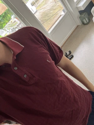 YSL Vinröd pikétröja - Snygg vinröd YSL pikétröja. Perfekt för en avslappnad men stilren look. Passar storlek S/M