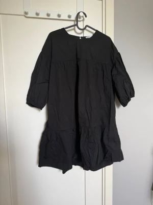 Svart volangklänning med trekvartsärm - En svart, luftig kortklänning med volangdetaljer och trekvartsärmar. Klänningen har en avslappnad passform och rund halsringning. Perfekt för dig som gillar enkel men trendig stil.🤗