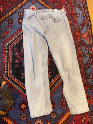 Ljusgrå raka jeans 34/32 - Säljer ett par klassiska ljusblå jeans från Levi's med rak passform och fem fickor. Jeansen har knappgylf och är tillverkade i denim. Perfekta för en avslappnad och trendig look.