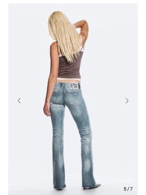 Cheap Monday ljusblå bootcut jeans - Säljer ett par ljusblå bootcut jeans från Cheap Monday med slitna detaljer och klassisk femficksmodell. Jeansen har en stor vit patch med Cheap Monday-loggan bak i midjan. Perfekta för en avslappnad och trendig look.