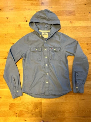 Vintage Hollister skjorta med knappar - Säljer nu en snygg skjorta från Hollister i blå med huva och snörning. Skick 8/10. Tröjan är i storlek M och modellen på bilden är 183 och väger 67 kilo. Skjortan saknar huv snöre. Skjortan som jag har på mig är samma modell och storlek fast med snöring.