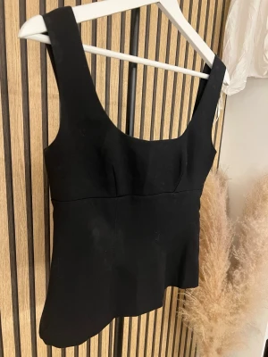 Svart linnetopp från h&m - Stilren svart linnetopp med breda axelband och figurnära passform. Toppen har en enkel, elegant design utan synliga detaljer eller mönster. Perfekt att matcha med jeans eller kjol för en clean look.