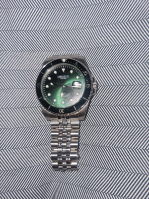 Dissing grön klocka i stål - Snygg klocka från Dissing med grön urtavla och silverfärgat armband i rostfritt stål. Klockan har tydliga indexmarkeringar, datumfönster och en vridbar svart bezel. Perfekt accessoar för dig som vill ha en stilren och modern look. Den är princip helt ny använd kanske 2-3 gånger ny pris är 1500-1900