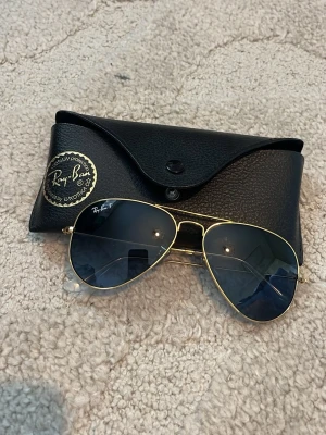 Ray-Ban aviator solglasögon guld/blå - Snygga Ray-Ban aviator solglasögon med tunna guldfärgade metallbågar och blåtonade glas. Klassisk pilotmodell som ger en tidlös look. Kommer med original svart Ray-Ban fodral. Köptes i Maldiverna på flygplatsen för ca 200€ men hittar tyvärr inte kvittot. Mycket bra skick. Hör av vid fundering.