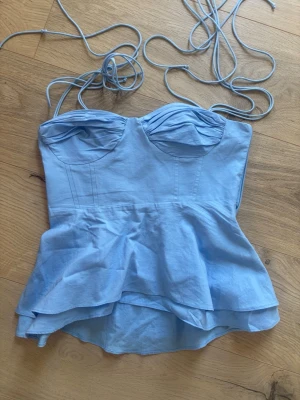 Ljusblå linnetopp från Zara Xs - Supersöt ljusblå linnetopp från Zara med tunna axelband och volang nedtill. Toppen har en figurnära passform med markerade kupor och en lätt peplum-effekt. Perfekt för varma dagar och snygg att styla med jeans eller kjol.