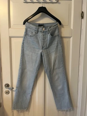 Snygga Ljusblå raka jeans  - Säljer ett par ljusblå jeans från Amisu med hög midja och raka ben. Jeansen har råa, fransiga benslut och klassisk femficksdesign. Tillverkade i denim med en avslappnad passform som ger en cool och trendig look.