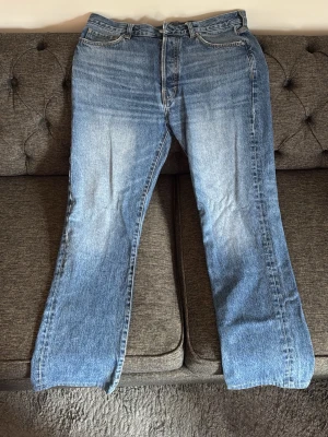 Blå raka jeans från taktill - Säljer ett par klassiska blå jeans från Taktill med rak passform och fem fickor. Jeansen har en snygg tvättad look med ljusare partier framtill och bak, samt en vit patch med logotyp bak i midjan. Perfekta för en avslappnad och trendig stil.