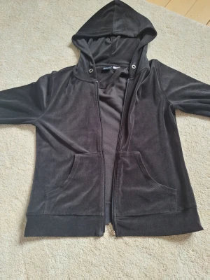Svart velour hoodie med dragkedja - Mjuk och skön svart hoodie i velour med dragkedja framtill och två fickor. Perfekt för en chill och avslappnad stil. Säljer för den inte används. Skön o mysig💕