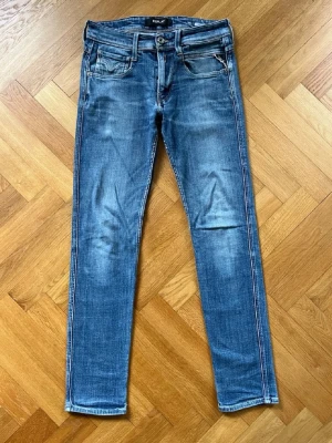 Blå slim fit jeans från Replay - Snygga blå slim fit jeans från Replay med klassisk femficksdesign och slitna detaljer. Jeansen har normal midja, smala ben och är gjorda i stretchigt denimtyg för extra komfort. Perfekta för en avslappnad och trendig look.