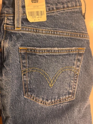 Levi's 501 blå raka jeans - Klassiska blå Levi's 501 jeans med raka ben och hög midja. Jeansen har fem fickor, gul kontrastsöm och ikonisk läderpatch bak i midjan. Tillverkade i slitstark denim som ger en tidlös look. Perfekta för dig som gillar vintagevibbar och streetstyle. Den är helt ny och är köpt från Levi's butiken 