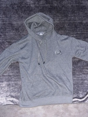 Grå hoodie från Christian Dior - Snygg grå hoodie från Christian Dior med broderad CD-logga på bröstet. Klassisk passform med huva och dragsnören samt känguruficka framtill. Tillverkad i mjukt material som känns skönt mot huden. Perfekt för en avslappnad och trendig look.