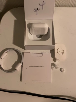 Apple AirPods Pro med laddningsetui - Säljer ett par vita Apple AirPods Pro med trådlöst laddningsetui. Hörlurarna har silikonproppar i olika storlekar, brusreducering och adaptivt ljudläge. Medföljer laddningskabel och originalförpackning. Snygg och kompakt design i plast.