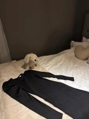 Svart långärmad klänning - Snygg svart långärmad klänning med figurnära passform. Klänningen har puffiga axlar och är i ett stretchigt, ribbat material som ger en modern look. Perfekt för dig som gillar stilrena och enkla plagg.