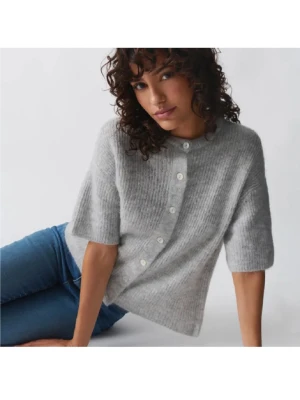 Grå stickad kofta Gina  - Mysig grå stickad kofta med korta ärmar och knäppning framtill med vita knappar. Koftan har en avslappnad passform och är tillverkad i ett mjukt, fluffigt material som ger en trendig look.