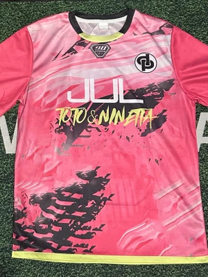 Rosa JUL x Toto & Nineta t-shirt - Unik rosa t-shirt från JUL x Toto & Nineta med coolt grafiskt tryck i svart och gult framtill. Nummer 7 och texten 'Nineta' på ryggen. Tillverkad i lätt och snabbtorkande material, perfekt för sport eller streetwear. Svart krage och gul detalj längst ner.