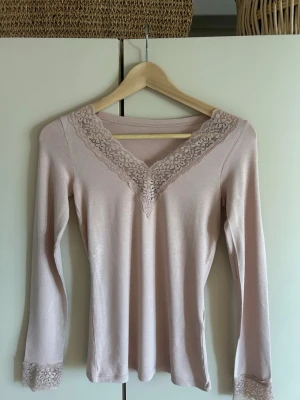 Ljusrosa långärmad  tröja  med spetsdetaljer. - Säljer en ljusrosa långärmad topp med v-ringning och fina spetsdetaljer runt halsen och ärmsluten.. Materialet är mjukt och stretchigt, vilket gör den bekväm att bära. Köpte den utomlands i Frankrike. Passar till  många tillfällen. (Pris går att diskutera) 💗