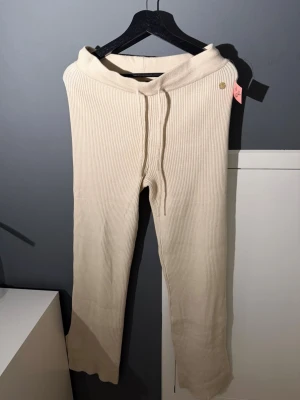 Beiga ribbade loungebyxor - Mysiga loungebyxor i beige ribbat material med dragsko i midjan och raka ben. Perfekta för chill dagar hemma. Byxorna har en mjuk och stretchig känsla och sitter skönt på kroppen.